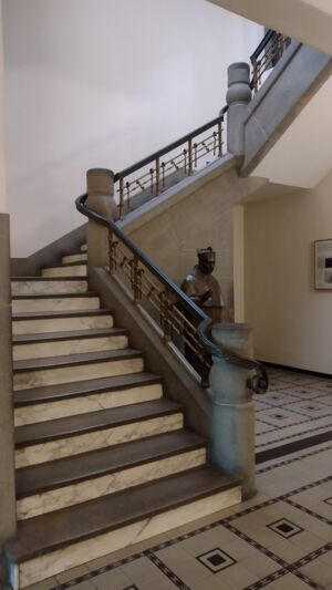 Ein Foto aus dem Borromäushaus. Man sieht die massive steinerne Treppe vom Erdgeschoss ins 1. Obergeschoss. Drei Treppenabschnitte sind durch zwei Plateaus unterbrochen.