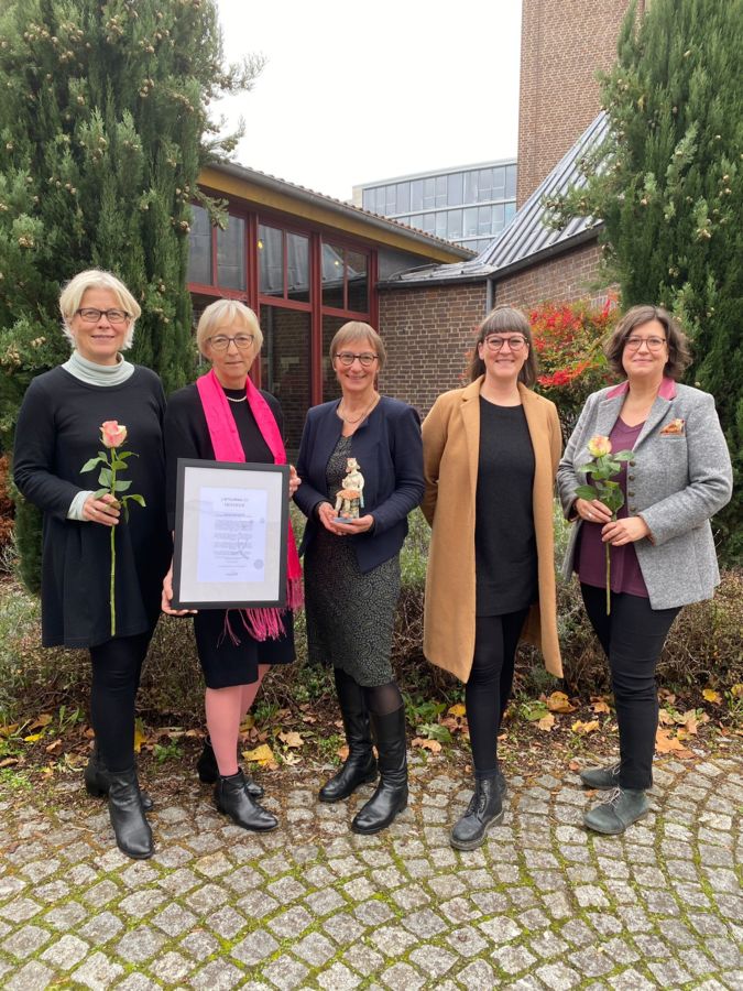 Auf dem Foto sind die Projektverantwortlichen von Women4Youth abgebildet. Sie halten Blumen, eine gerahmte Urkunde sowie den Preis in der Hand.
