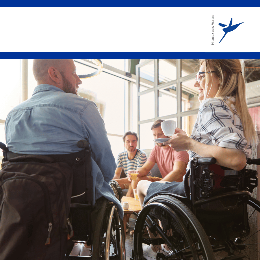 Vier Personen sitzen in einem Café mit Tassen in der Hand. Zwei von ihnen nutzen einen Rollstuhl.