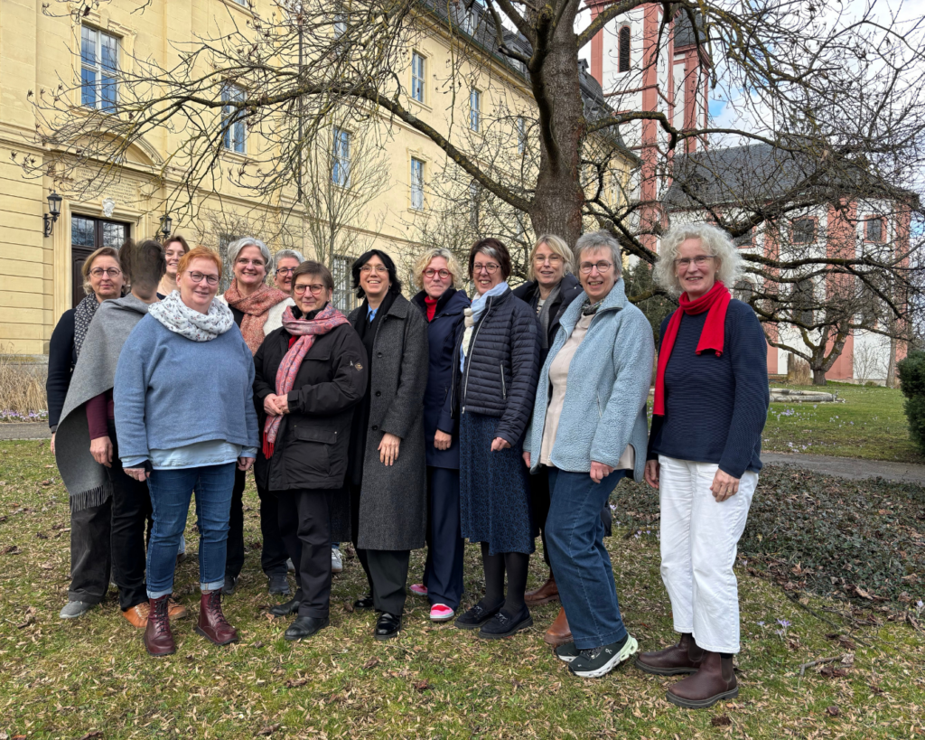 13 Frauen stehen auf einer Wiese vor einem gelben Gebäude (Mutterhaus des Kloster Oberzells).